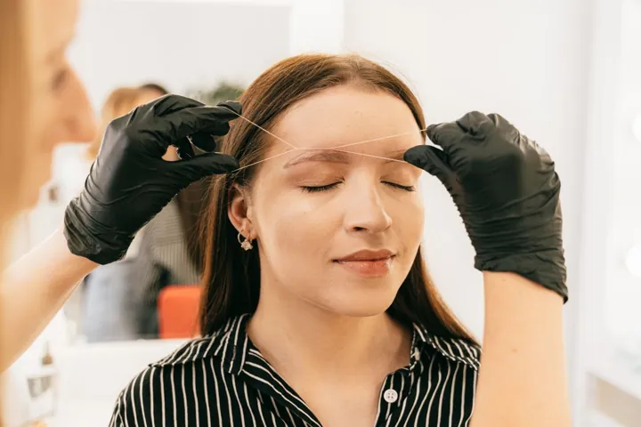 A beauty professional grooming a client's brows